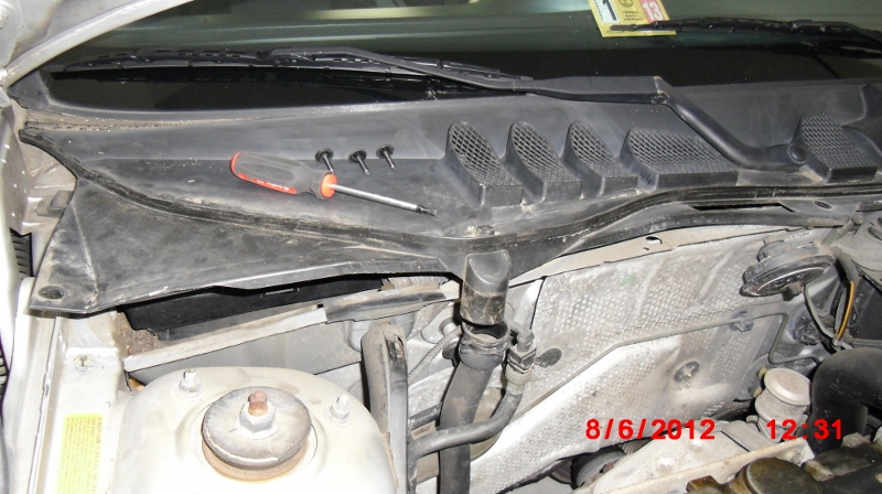 Removed 3 screws with a size T25 and loosened drain hose in order to lift the passenger side of the rain guard at the rear of the engine compartment.