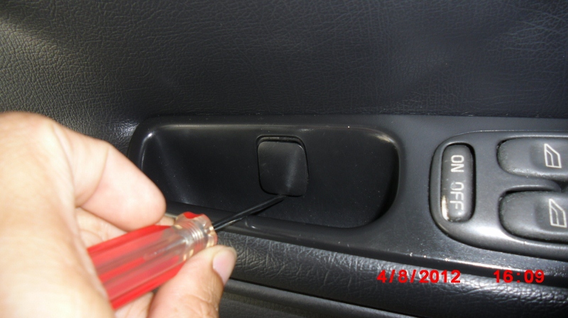 Use a small flat-blade screwdriver to pop off the screw cover of the interior door trim of a 1998 V70 XC.