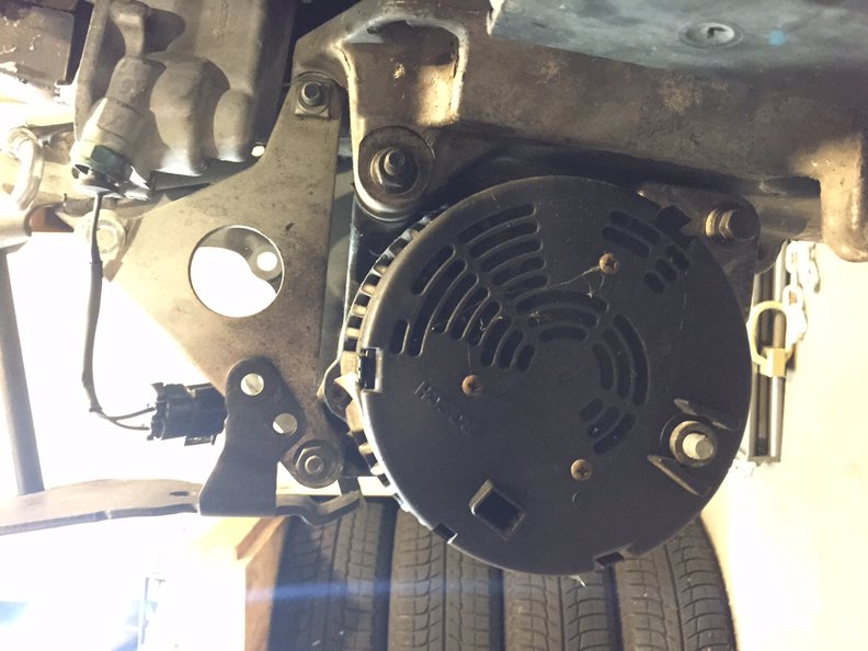 Alternator from the back, all mounted up, by 3 bolts. The longest bolt is at 4:30 or 5 o'clock, you can see the head because it comes in from the back side of the alt. Then the next longest bolt is the one at 2 o'clock, coming in from the serp belt side so you can only see the 13 mm nut here (the 12 mm head is recessed in the hole visible in the first photo). Then the final alternator bolt is at 11 o'clock, again you can see a 13 mm nut because the 12 mm head is over on the serp belt side pump side (visible in first photo).