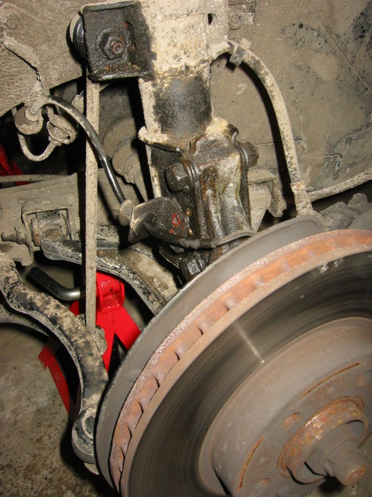 First, jack the front up and support it on jack stands (1 on each side).  The jack stands are positioned on the sub frame of the Volvo (check your manual to see where it is safe to put jacks under the car).  The sub frame runs around the front end of the car.  Block the rear wheels and remove the front wheels.