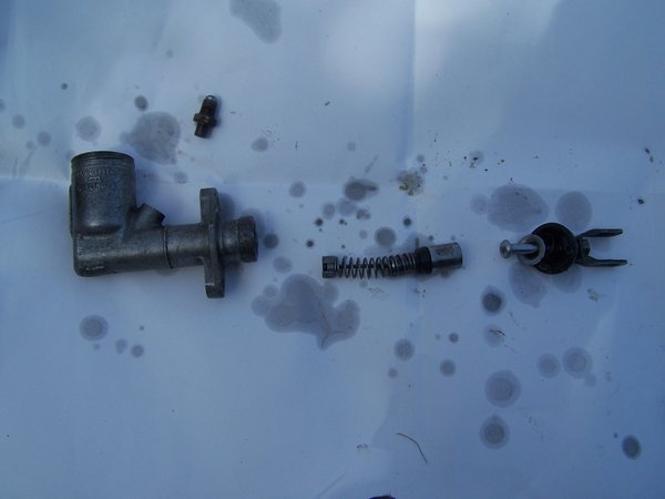 Here is what the guts of the cylinder looked like. It was a pain in the &amp;$$ getting it apart. The biggest problem seems to be lack of knowledge on my part...... I did admit in an earlier post that I'm not a car guy. Just imagine a confused ape holding the cylinder in hand and scratching his head with the other. Okay, back to the car.... There is a spring keeper ring under the dust cover thingy that removes easily. When you pull the pin, everything on the right side of the pic pops out (piece of cake!). It allows you access to the little piston inside. This is the confusing part..... you can press on the piston and it springs back and forth, but doesn't come out. I go inside and grab my $45 rebuild kit (the little plastic bag that feels just like a free toy in a Happy Meal.... I got screwed on that one). And the $45 kit didn't even have any instructions. Google was my next option...... no help there. I'm on my own here. I lube everything up, and even remove the little fitting on top thinking that it would help, it didn't. That damn little piston is pissing me off now! So with some cussing (and I'm ashamed to say, a few tears) I start working the piston like crazy. After 5 minutes, I noticed the piston is now traveling to the edge of the cylinder housing! Another minute and she's out! The center portion in the photo is out and ready to rebuild. I used some wd40 and thoroughly cleaned all the parts. I rebuilt the cylinder and threw it back on the car.<br /><br />Bleeding the cylinder required opening the fitting on the top of the master. I am sharing this valuable information with you free of charge. Trust me..... after 20 minutes of pumping the clutch (thanks to my impatient 11 year old son), and opening and closing the bleeder valve on the slave (under the car), we realized that the air trapped in the top bend of the tubing would only come out after you crack the top fitting......<br /><br />....your welcome.
