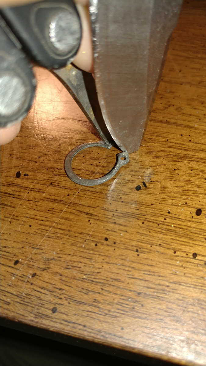 NOTE the spring clip with 2 holes in it. Brace 1 side and use a skinny prying tool to pry other side to remove clip from tumbler assembly.