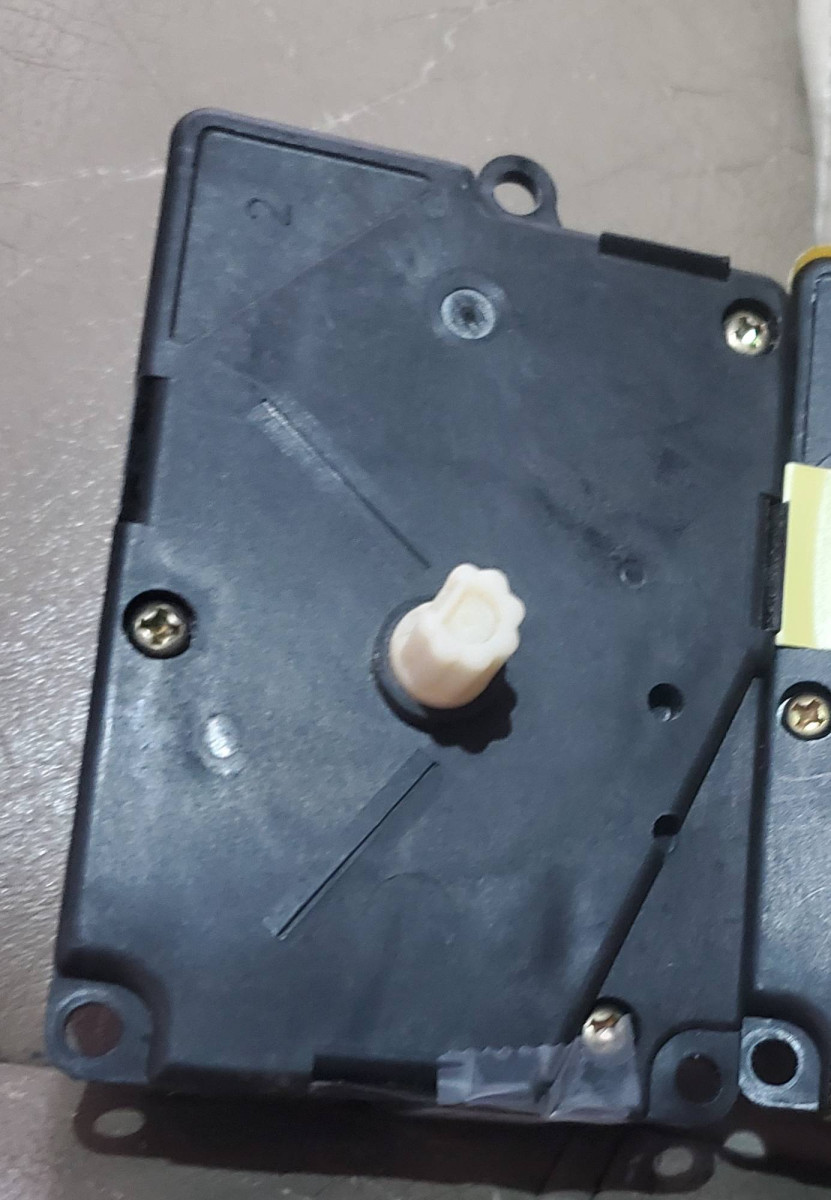 Motor showing white plastic shaft with splines and flat side.  Note three mounting screw holes, one top, two bottom.